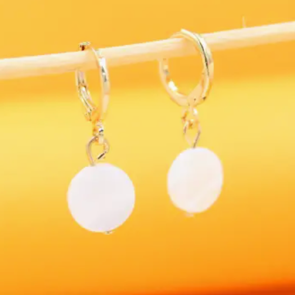 Gold earrings with white round stones on a yellow background