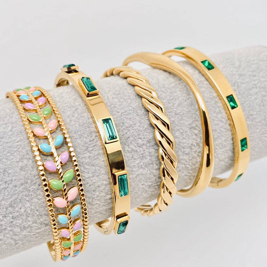 Three gold bracelets with green gemstones on a gray surface