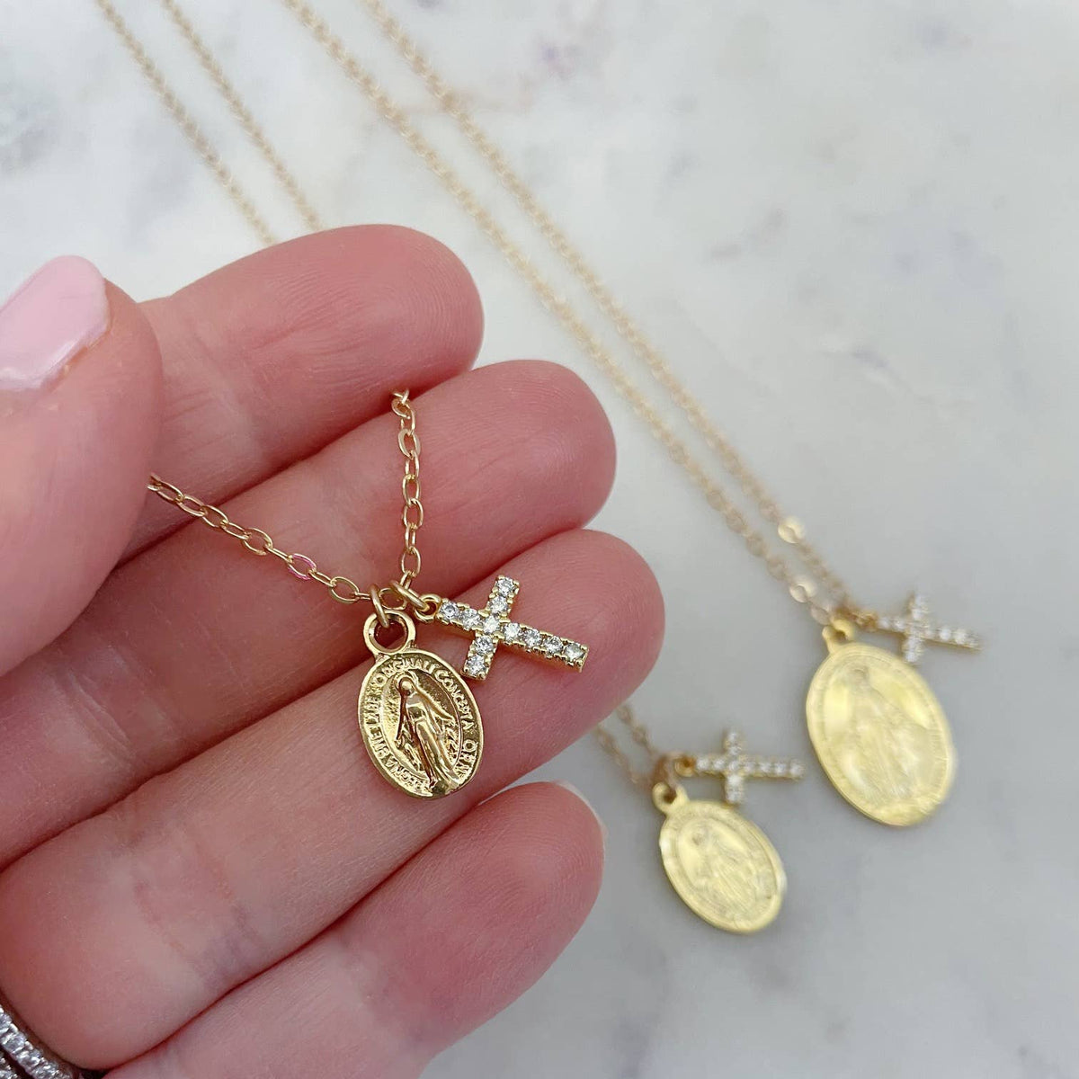 Gold necklaces with religious pendants held by a hand on a marble background