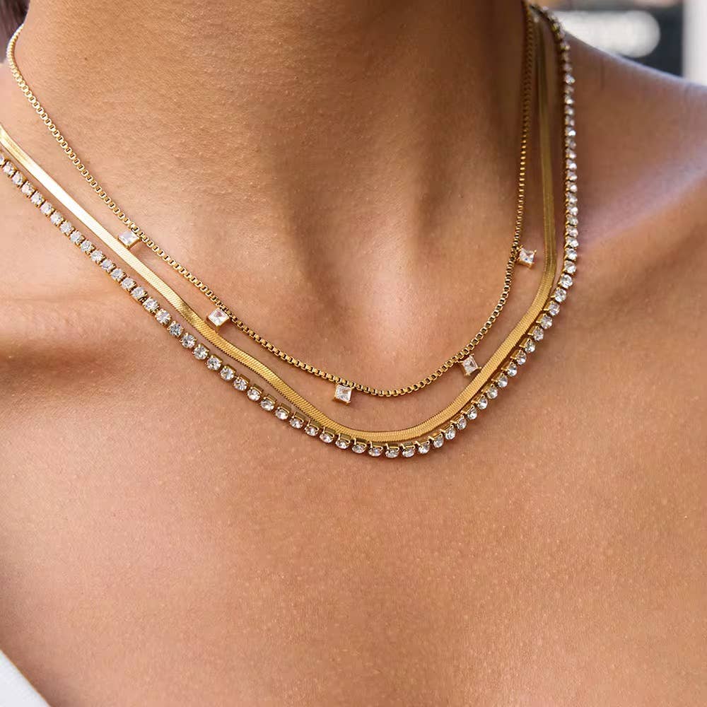 Close-up of a person wearing two gold necklaces with small diamonds on a blurred background