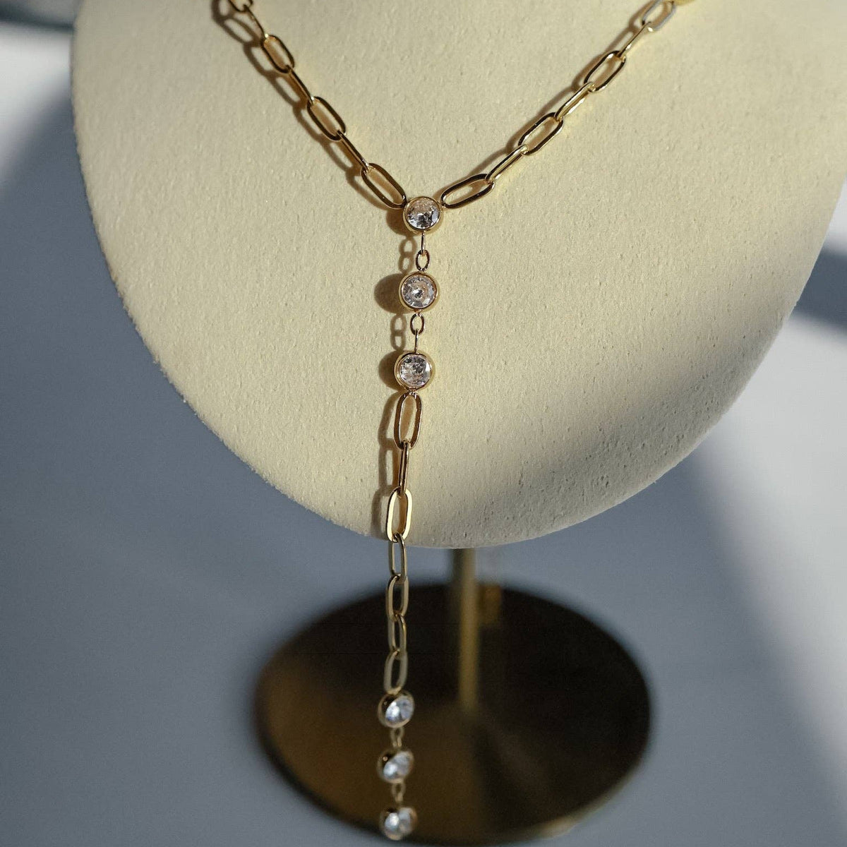 A gold Y-necklace with clear crystal accents and pearl-like drops, displayed on a cream-colored jewelry bust.