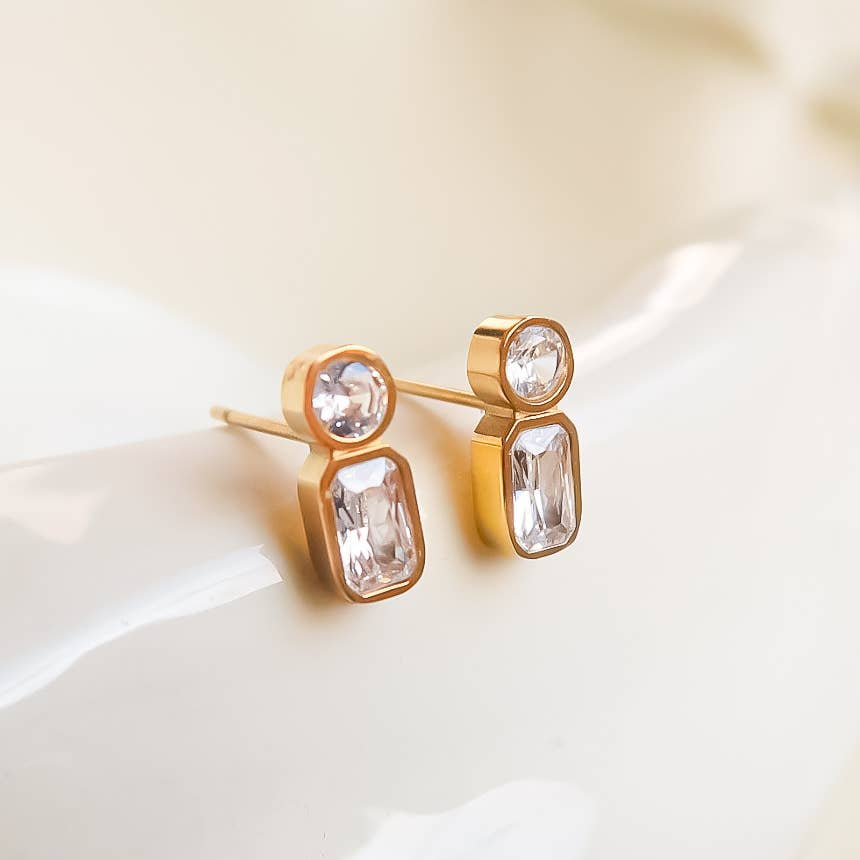 Gold earrings with clear gemstones on a white surface