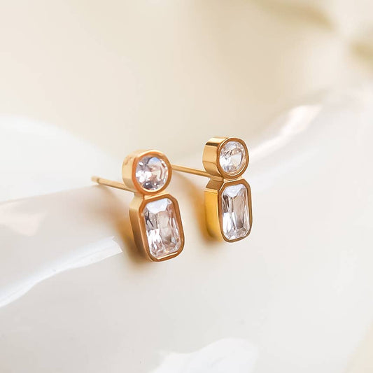 Gold earrings with clear gemstones on a white surface