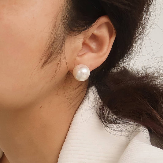 Close-up of a person wearing pearl earrings with a neutral background