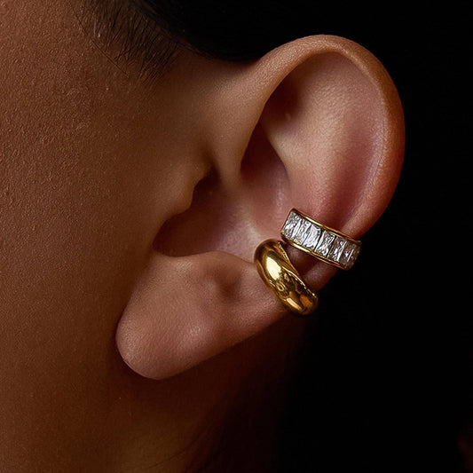 Close-up of an ear wearing two gold earrings with a dark background